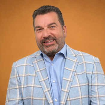 Portrait de Dominique Salgado, secrétaire. Homme aux cheveux foncés légèrement grisonnants et à la barbe poivre et sel soigneusement taillée. Il porte une chemise bleu pâle sous un veston à carreaux bleu clair et affiche un sourire chaleureux. Photographie utilisée pour la présentation des membres du Conseil d’administration.