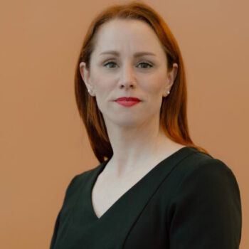 Portrait de Lucie Nault, administratrice. Femme aux longs cheveux rouge détachés tombant sous les épaules, portant un haut noir et de petites boucles d’oreilles. Elle regarde l’objectif avec une expression calme et professionnelle. Photographie utilisée pour la présentation des membres du Conseil d’administration.