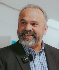 Portrait de Vincent Martin, administrateur. Homme aux cheveux gris très courts et à la barbe poivre et sel soigneusement taillée. Il porte une veste foncée sur une chemise à carreaux bleu et blanc et affiche un sourire chaleureux. Photographie utilisée pour la présentation des membres du Conseil d’administration.